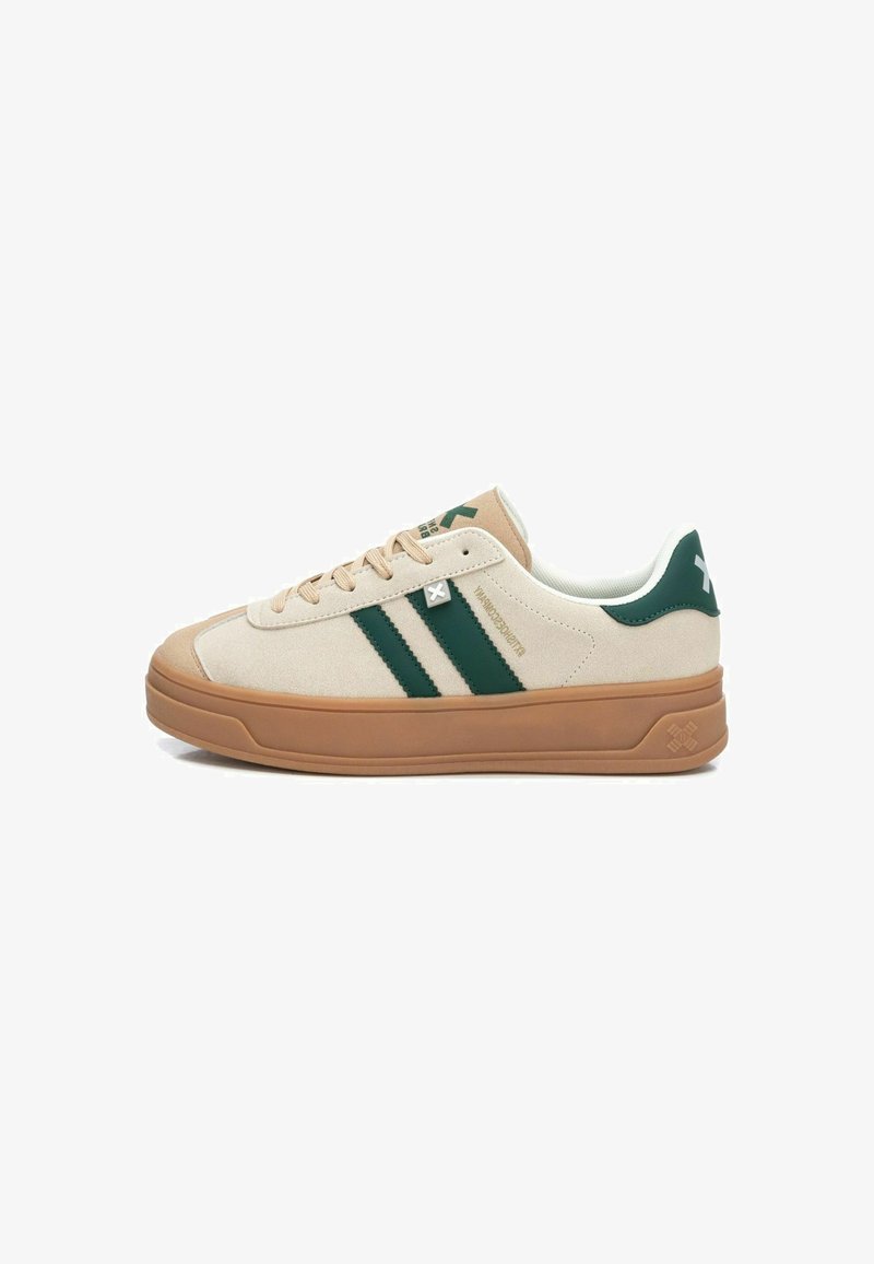 Zapatillas de ante beige con rayas verdes, suela de goma y cuello acolchado. Presenta un logo cerca de los cordones y acentos texturizados en la suela.