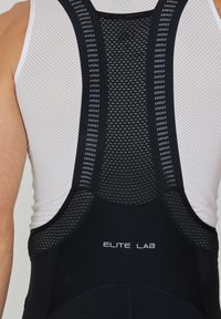 Schwarze Radler-Trägershorts mit strukturierten Mesh-Einsätzen und weißen Akzenten. Mit Branding "ELITE LAB" auf der Rückseite. Hergestellt aus leichtem, atmungsaktivem Material.