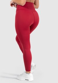 Leggings rojos de cintura alta fabricados en un material elástico, con una textura suave y un diseño ajustado. Combinados con zapatillas deportivas blancas.