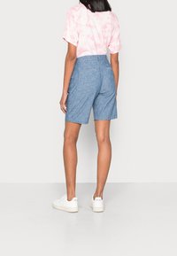 Shorts azules claros hasta las rodillas con bolsillos traseros, combinados con una camiseta rosa tie-dye. Zapatillas blancas completan el atuendo.