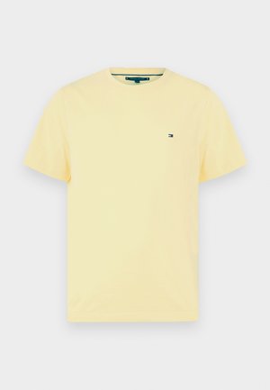 Helele kollane lühikeste varrukatega ümara kaelusega T-särk, millel on vasakul rinnal väike Tommy Hilfigeri lipu logo, taustal lihtne taust.