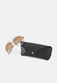 Óculos de sol com armação de metal prata, lentes castanhas em degrade e acabamentos castanhos. Acompanhados de uma capa protetora preta com fecho de botão.