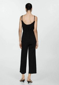 Svart jumpsuit med lös passform och vida ben. Tunna justerbara remmar och cinchad midja. Slät textur med en minimalistisk design.