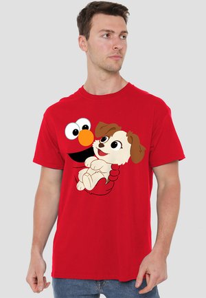 Red cotton t-shirt featuring a cartoon graphic of Elmo holding a small dog. Round neckline and short sleeves. Soft texture.