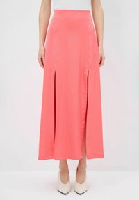 Gonna maxi di corallo realizzata in tessuto leggero, con due spacchi laterali, vita aderente e texture liscia. Indossata con tacchi a punta beige.