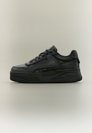 Sort lavtop sneaker med tyk gummisål, snørelukning foran og syninger i læderpaneler, vist i profil på neutral baggrund.