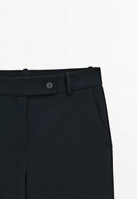 Mustat mittatilaustyönä valmistetut housut, joissa on sileä pinta, vyölenkit, etutaskut ja yksi nappikiinnitys vyötäröllä.