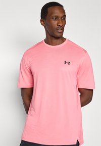 Αθλητική ροζ κοντομάνικη μπλούζα με υφή υφάσματος, λαιμόκοψη τύπου crew και μαύρο λογότυπο στο αριστερό πάνω μέρος του στήθους.