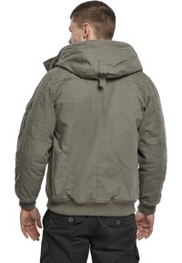 Olivgrüne Bomberjacke mit Kapuze, gerippten Bündchen und Saum. Verfügt über eine sichtbare Nahtstruktur und seitliche Taschen.