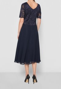 Marindräkt med spetsliv, korta ärmar, en flödande chiffonskjol och v-formad ryggdesign. Bärs med svarta högklackade skor.