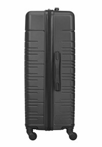 Duża czarna walizka z twardą obudową, wyposażona w cztery obrotowe kółka i centralny zamek błyskawiczny, pokazana w pozycji stojącej.