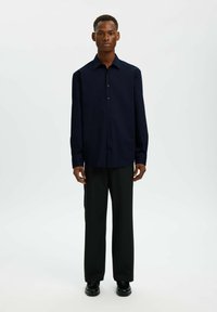 Chemise boutonnée bleu marine foncé avec un col pointu, manches longues et coupe décontractée, associée à un pantalon noir et des chaussures noires.
