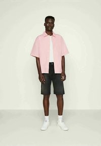 Short-sleeve light pink button-up shirt over a white T-shirt, paired with dark denim shorts and white sneakers.