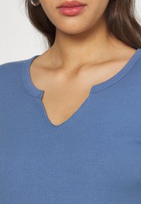 Top blu chiaro a coste con scollatura leggermente a V e maniche corte, che mette in mostra una sottile texture e un tessuto morbido e elasticizzato.