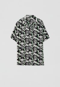 Chemise à manches courtes noire avec un motif graphique d'yeux et de bouches en blanc et vert. Dotée d'un col classique et d'une coupe décontractée.