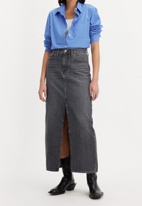 Modrá košile s knoflíky, bílý top pod ní, spárována se šedou džínovou maxi sukni s předním rozparkem a nošena s černými kotníkovými botami.