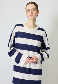 Pulover în dungi, de culoare bleumarin și crem, cu un design lejer, mansete largi și guler rotund, fabricat dintr-un material tricotat moale.