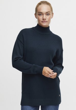 Mørk marineblå høyhalset genser, laget av mykt strikket materiale, med en avslappet passform og ribbede mansjetter, som har en liten logoaccent ved kanten.