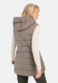 Hættevest i taupe med quiltet tekstur. Har en mellemlang længde og sidelommer, bæres over en lys top.