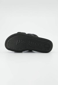 Semelle de chaussure en caoutchouc noir présentant une texture, un motif de grip avec des points en relief et un logo. Forme arrondie avec un bord renforcé.