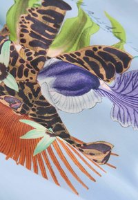 Tissu à motif floral et feuillu avec des touches imprimées léopard en vert, orange, violet et noir sur fond bleu clair.