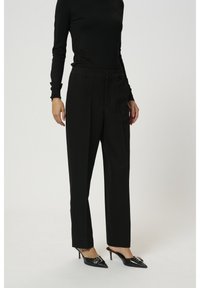 Černé kalhoty na míru s rovnými nohavicemi, hladkým povrchem a postranními kapsami, doplněné černými špičatými podpatky.