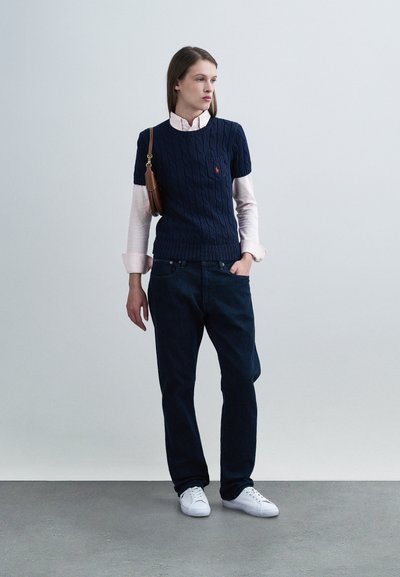 Laivastonsininen palmikkoneulepusero lyhyillä hihoilla vaaleanpunaisen pitkähihainen paidan päällä, tummat farkut, valkoiset tennarit ja ruskea olkalaukku.