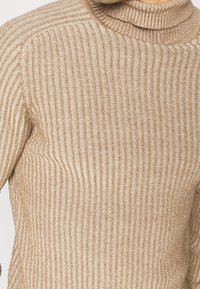 Beiger, gerippter Strickpullover mit hohem Ausschnitt und langen Ärmeln, mit glatter Textur und dezentem Glanz.