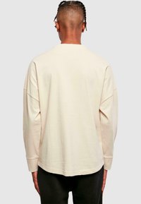 Light beige long-sleeve shirt with a relaxed fit, round neck, and dropped shoulders; smooth texture and round hem.