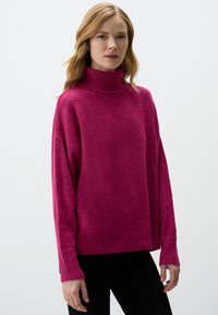 Pull à col roulé fuchsia en tricot doux et texturé, avec des poignets et un ourlet côtelés, une coupe décontractée et des épaules tombantes.