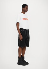 White cotton t-shirt with "icecream" print in yellow and pink, paired with black denim shorts featuring white stitching and functional pockets. Black boots.