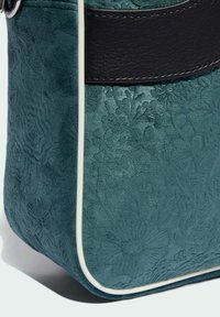 Sac à main gaufré turquoise avec des motifs floraux, présentant un accent en cuir noir et un passepoil blanc le long des bords. Détails de surface texturée visibles.