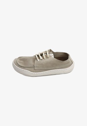 Zapato casual tipo slip-on con parte superior de ante beige, cordones blancos y suela de goma blanca, mostrado de lado sobre un fondo blanco.