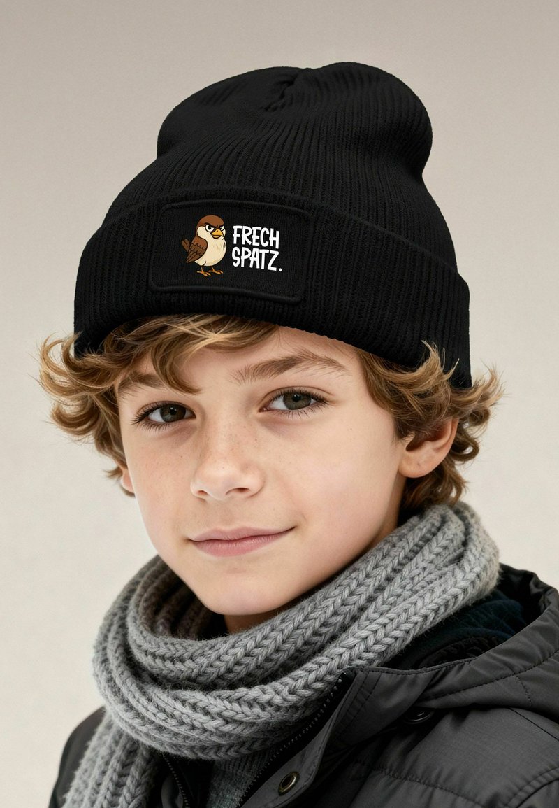 Black knitted beanie featuring a patch with a cartoon bird and "FRECH SPATZ" text. Accompanied by a textured gray scarf.