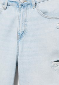 Jean en denim bleu clair avec poches avant, bouton en métal, passants de ceinture et un détail déchiré sur la cuisse droite.