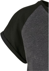 T-shirt à manches courtes avec corps gris foncé et manches raglan noires, avec un revers roulé sur la manche.