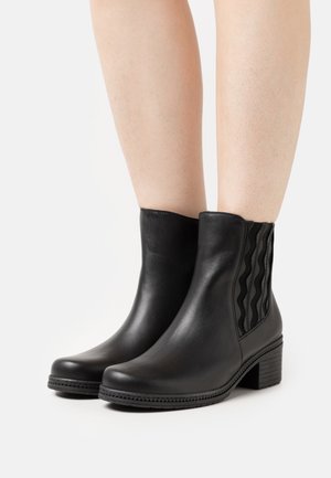 Black leather ankle boots with a smooth surface, elastic side panels featuring wavy patterns, and a low block heel for stability.