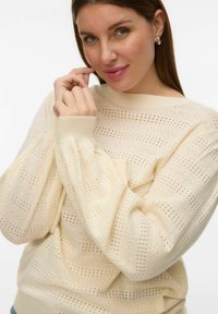 Pull en maille crème clair avec un motif texturé à mailles ouvertes, poignets côtelés et coupe décontractée. Idéal pour superposer ou porter au quotidien.
