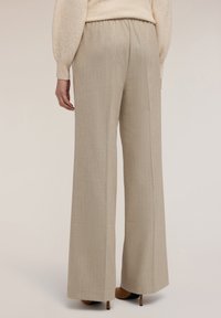 Beige kalhoty s širokými nohavicemi a texturovaným vzorem, elastickým pasem a délkou ke kotníkům. Nohavice hladce spadají, což zvyšuje přizpůsobený vzhled.