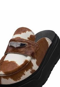 Slip-on sko med brunt og hvidt kvægskinds mønster, tyk sort sål og metal Air Jordan logo på den forreste rem.