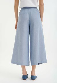 Lichtblauwe, wijde culottes van een gestructureerde stof. Heeft een hoge taille, twee achterzakken en een ontspannen silhouet. Gecombineerd met blauwe schoenen.