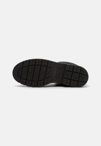 Suela de zapato negra con patrón de agarre texturizado y "HILFIGER" embellecido en la sección media, fotografiado sobre un fondo blanco.