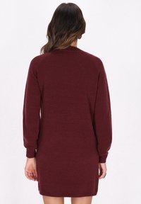 Burgunderfarbener Strickpullover-Kleid mit langen Ärmeln, gerippten Bündchen und einer leicht taillierten Form. Weiche Textur und Seitenschlitz-Details.