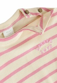 Top per bambini a righe in crema e rosa. Presenta una texture a costine, colletto corto e chiusura con due bottoni. "Whole Love" ricamato in rosa.