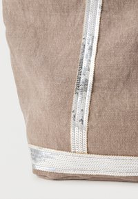 Μπεζ υφασμάτινη τσάντα tote με ασημί παγιέτες κατά μήκος δύο κάθετων ραβδώσεων και μιας οριζόντιας ζώνης στη βάση για επιπλέον λεπτομέρεια.