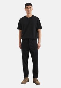 Black cotton T-shirt paired with black elastic-waist trousers featuring side seam details, complemented by light brown textured boots.