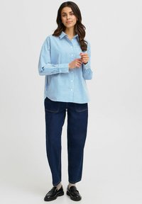 Blue and white striped button-up shirt with long sleeves, paired with dark blue denim pants and black loafers. Simple design and relaxed fit.