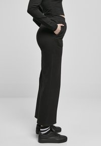 Zwarte, elastische broek met zijzakken, aansluitend bij de taille en uitlopend naar de onderkant, gecombineerd met zwarte sneakers en gestreepte sokken.