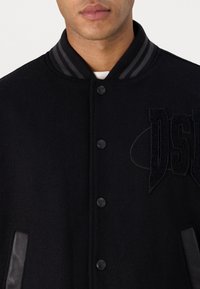 Veste noire en mélange de laine avec col côtelé, fermeture par bouton, accents en cuir et logo "DSQUARED2" embossé sur le devant.