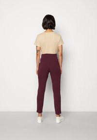 Beige t-shirt, kort ärm, kombinerad med högmidjade, vinröda byxor. Byxorna sitter åtsittande genom benen med en jämn yta och minimal design.